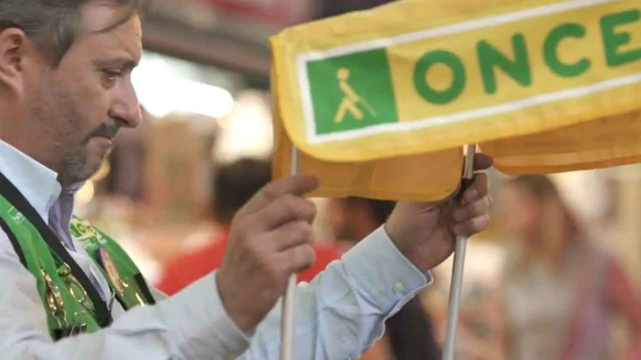Trabajador de la ONCE con el uniforme de vendedor ajustando un puesto de venta de cupones de la organización. Copiar