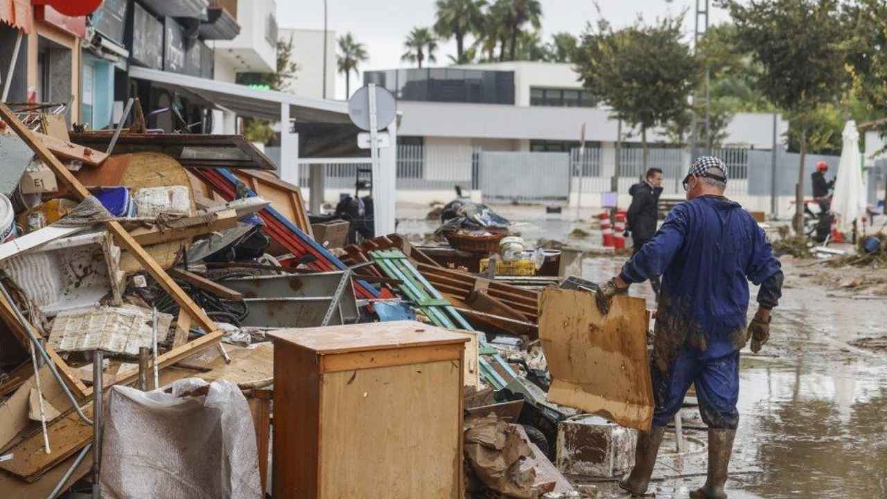 Un hombre retira muebles y enseres dañados por una inundación en una calle embarrada tras una DANA.