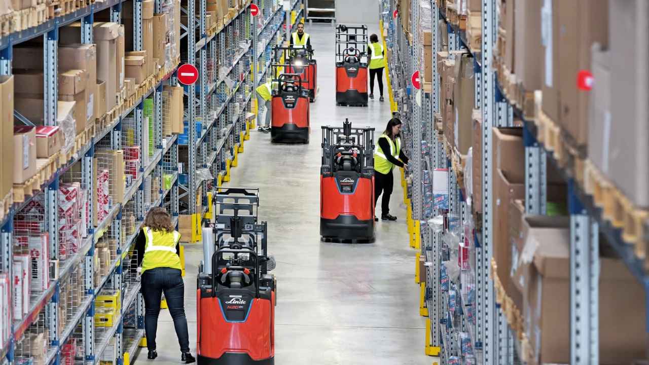 Trabajadores preparando pedidos en un almacén logístico con estanterías y carretillas eléctricas