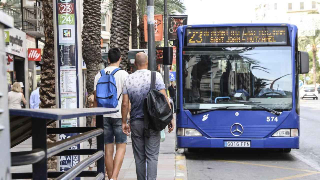 Autobús urbano de la línea 23 de Alicante detenido en una parada con varios pasajeros junto al vehículo