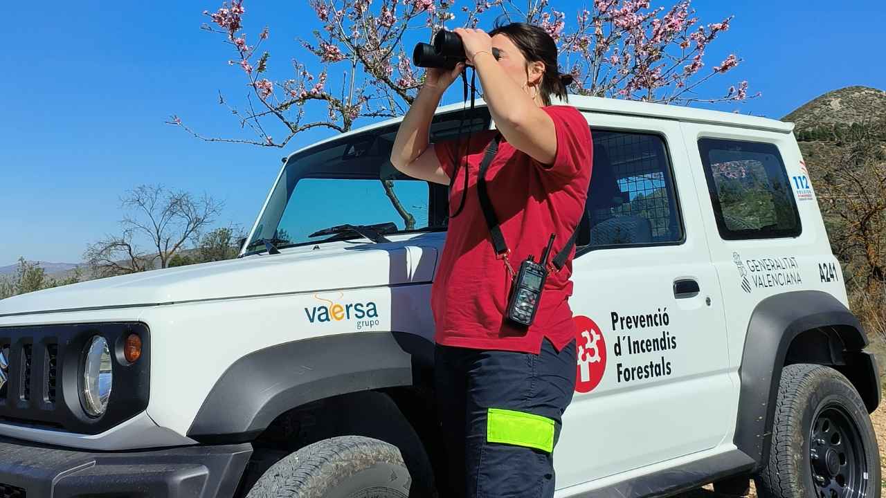 Trabajadora de prevención de incendios forestales observando el monte con prismáticos junto a un vehículo de VAERSA en la Comunidad Valenciana.