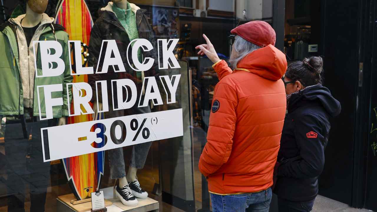Dos personas observan un escaparate de ropa con descuentos del 30% anunciados por el Black Friday.