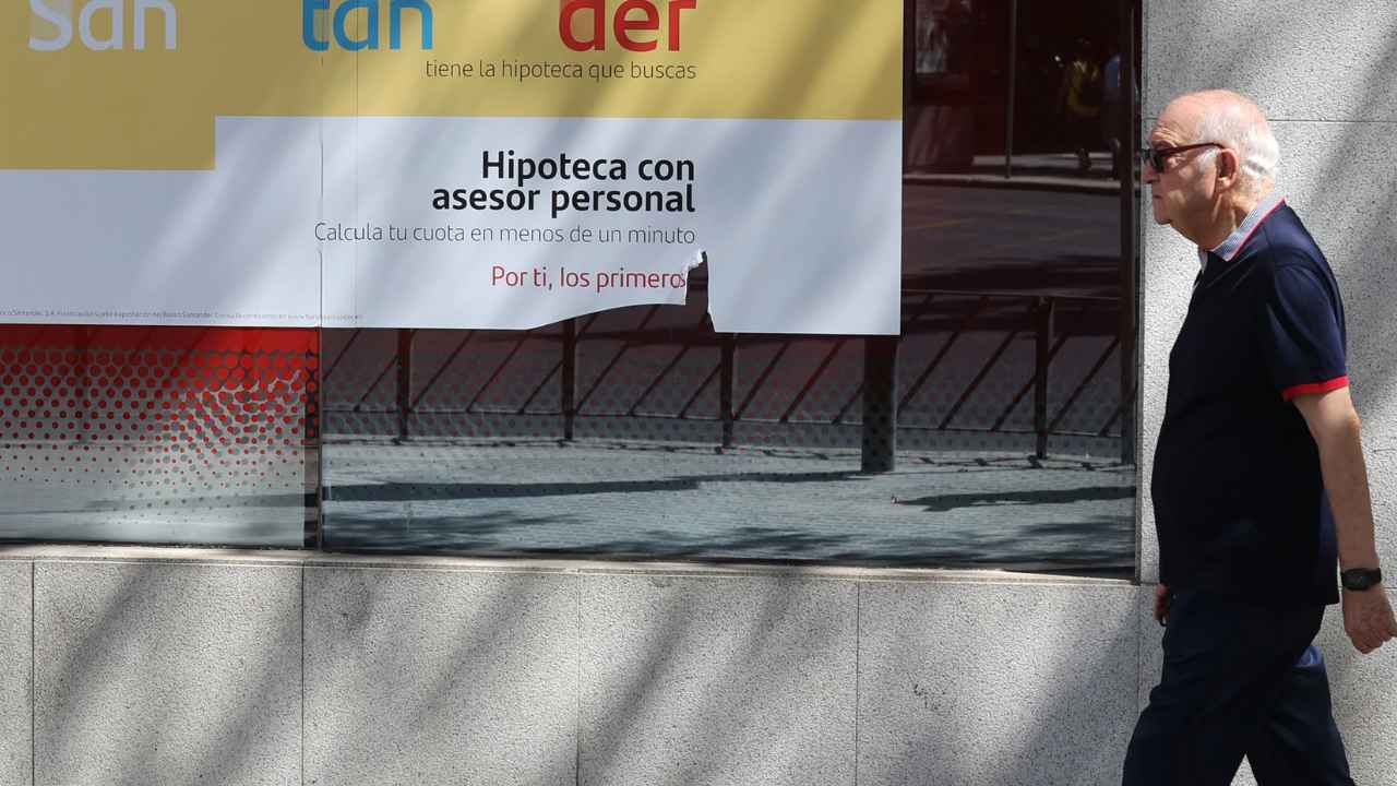 Un hombre camina frente a una oficina del Banco Santander con publicidad de hipotecas, imagen del mercado hipotecario español.