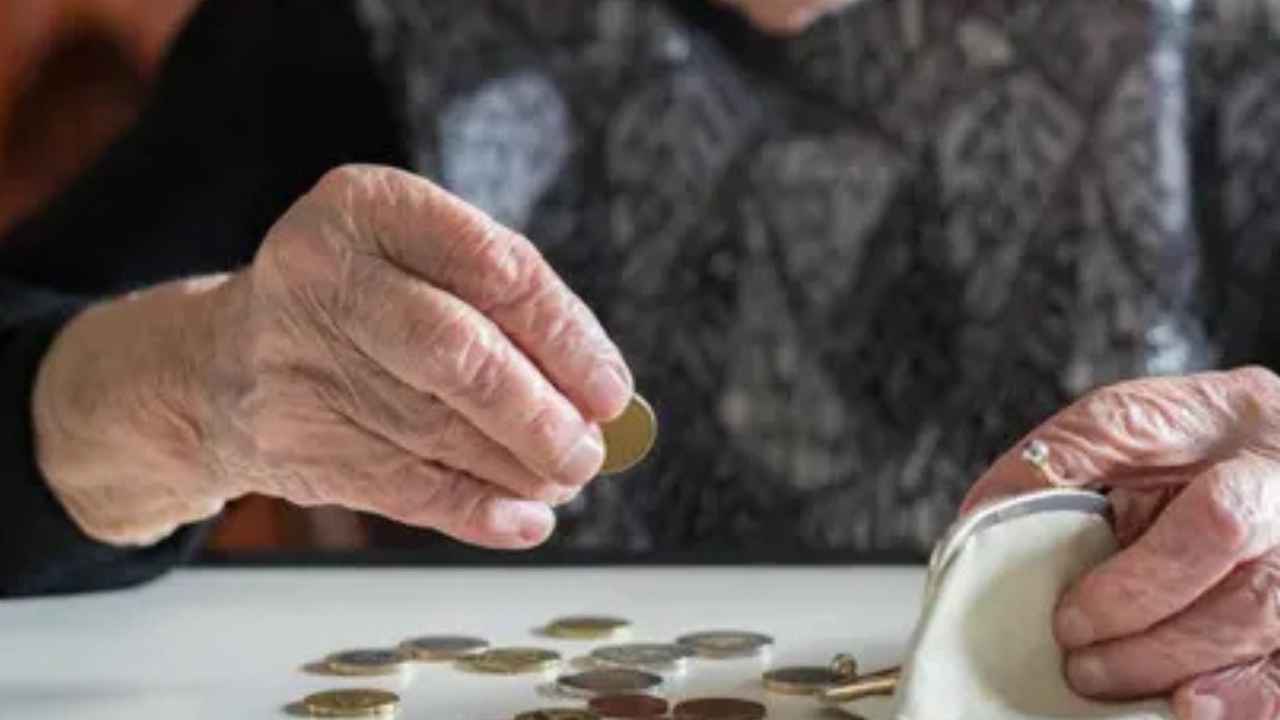 Mujer mayor contando monedas sobre una mesa junto a un monedero, imagen ilustrativa de una pensión de viudedad.